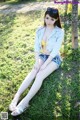 A woman sitting on the grass in a yellow bikini top and denim shorts.