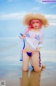 A woman in a bikini and straw hat on the beach.