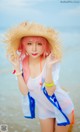 A woman with pink hair wearing a straw hat on the beach.