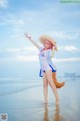 A woman in a bikini and hat standing on a beach.