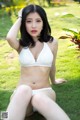 A woman in a white bikini sitting on the grass.