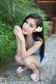 A woman in a blue and white dress crouching down with a flower in her hair.