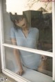 A woman in a blue bodysuit leaning against a window.