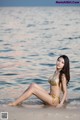 A woman in a gold bikini sitting on the beach.