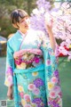 A woman in a blue and pink kimono standing next to a tree.