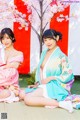 Two women in kimonos sitting next to each other under a tree.