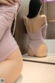 A woman in a pink bodysuit is looking at herself in the mirror.