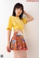 A young woman wearing a yellow top and a colorful skirt.