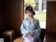 A woman in a blue kimono sitting on a wooden table.