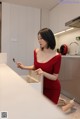 A woman in a red dress sitting at a kitchen counter.