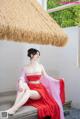 A woman in a red dress sitting on a wooden bench.