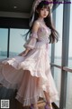 a woman in a pink dress and hat standing by a window