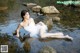 A woman in a white dress sitting on a rock in the water.