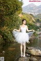 A woman in a white dress standing on a rock by a river.