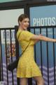 A woman in a yellow dress posing in front of a fence.