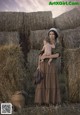 A woman holding a baby in front of hay bales.