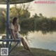 A woman sitting on a bench under an umbrella by the water.