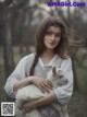 A woman holding a white goat in a forest.