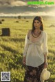 A woman standing in a field holding a straw hat.