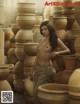 A naked woman standing in front of a pile of clay pots.