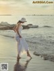 A woman in a white dress and hat walking on the beach.