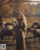 A woman standing in front of a herd of sheep.