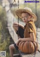 A young boy sitting on a wooden bench with a pumpkin.