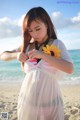 A woman in a white dress holding a sunflower on the beach.