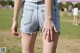 A woman in a white shirt and blue denim shorts.