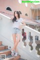 A woman in a white shirt and denim shorts posing on a stairway.