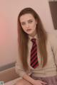 A woman in a school uniform sitting on a bed.