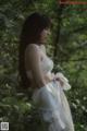 A woman in a white dress standing in the woods.