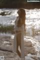 A woman in a white robe standing by the water.