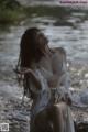 A woman in a white lingerie sitting on a rock by the water.