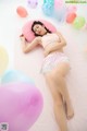 A woman laying on a pink pillow surrounded by balloons.