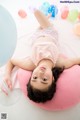 A little girl laying on a pink pillow with balloons.