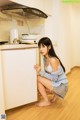 A woman crouching down in a kitchen next to a refrigerator.