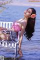 A woman in a pink bikini sitting on a white chair in the water.